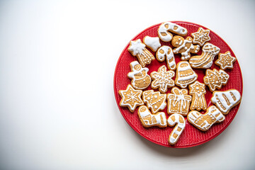 Christmas homemade gingerbread cookies of different shapes decorated with white icing laying on red plate on white background. Festive flatlay with negative space