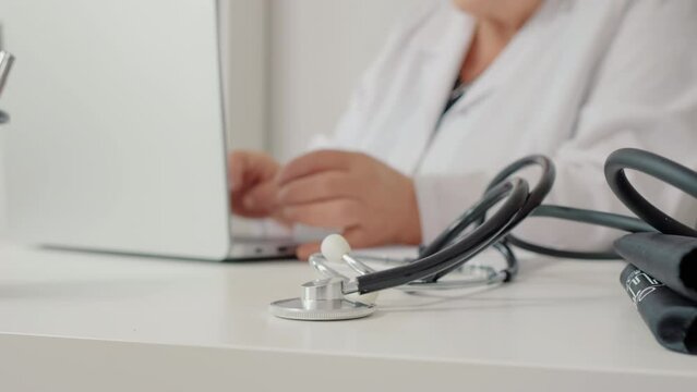 Closeup Stethoscope with doctor reading research report background on laptop in hospital. Selective focus woman doctor working on computer and medical equipment in front.