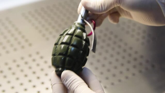 Hands in rubber gloves spin a hand grenade