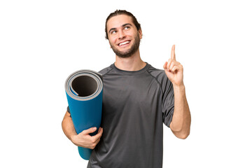 Young sport man going to yoga classes while holding a mat over isolated background pointing up a...