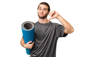 Young sport man going to yoga classes while holding a mat over isolated background showing thumb...