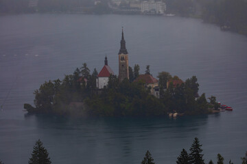 Aerial view of Island in Bled Lake, with Bled city in background. Church and other buildings in the...