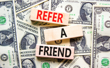 Refer a friend symbol. Concept words Refer a friend on wooden blocks on a beautiful background from dollar bills. Business and refer a friend concept. Copy space. - obrazy, fototapety, plakaty