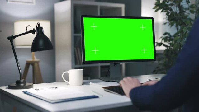 Businessman in formal clothes working on computer with chroma screen, blank green copy space in evening office interior