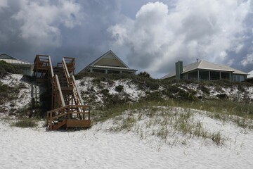 Upscale beach homes above white sand and metallic stairways under a stormy sky in Florida