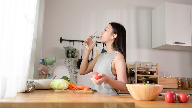An Asian young woman drinking fresh water in kitchen at home , healthy lifestyle concept