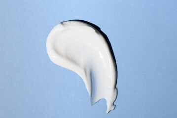 Liquid white cream smear isolated on blue background. Beauty cosmetic smudge such as hair conditioner, creamy lotion, facial retinol serum, mask balm, cleanser, shower gel or shampoo top view