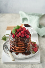 Chocolate Pancakes. Pancakes with fresh raspberry with chocolate glaze or toppings in gray bowl on light gray table background. Homemade classic american pancakes. Page for magazine concept.