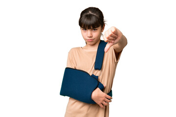 Little caucasian girl with broken arm and wearing a sling over isolated background showing thumb down with negative expression