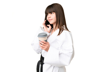 Little Caucasian girl doing karate over isolated background holding coffee to take away and a mobile