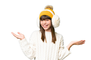 Little caucasian girl wearing winter muffs over isolated background with shocked facial expression