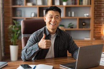 Glad adult asian man ceo manager show thumb up gesture at table with laptop in office home interior