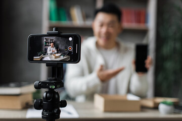 Focus on screen of smartphone, pleasant asian man filming video on modern phone camera while opening parcel box with new smartphone. Concept of people, technology and blogging.