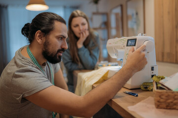 A man sews on a sewing machine, a woman explains how to sew. Family home hobby.