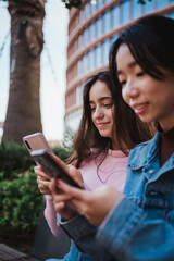 Two friends sending text messages to friends on their smart phones while they are sitting