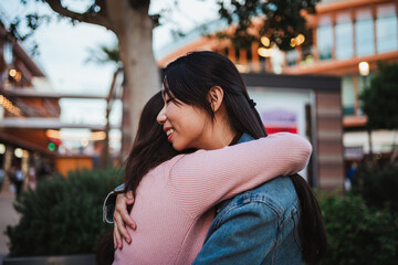 Fototapeta premium Two laughing young women hugging each other at a shopping center