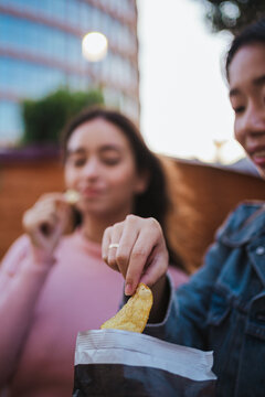 Close Up Shot Of Two Young Women Eating Chips From A Bag While They Have Fun