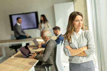 Young business woman at startup office with arms crossed in front of her colleagues as team leader