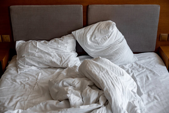 pillows and blankets lie on the bed in an improper form; unmade bedding on the bed; white bed linen