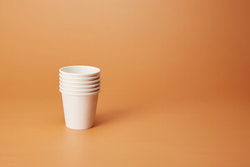 Disposable white stack of recyclable cardboard paper cups isolated on the bright solid fond plain...