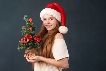 happy girl in a new year cap for christmas with a tree in her hands.