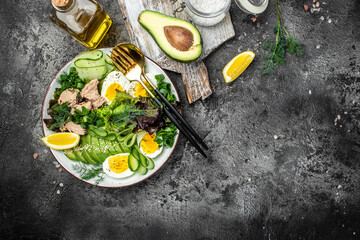 Obraz na płótnie Canvas Diet salad with tuna, avocado, egg, cucumber and fresh salad on a dark background, Ketogenic diet. Healthy food concept, top view