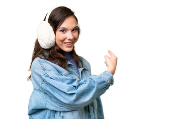 Young caucasian woman wearing winter muffs over isolated background pointing back