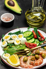 Ketogenic diet breakfast shrimps, prawns, soft fried egg, fresh salad, tomatoes, cucumbers and avocado on a dark background. Keto, paleo lunch. vertical image. top view