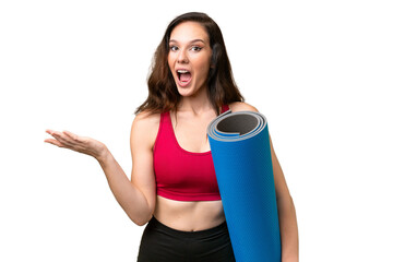 Young sport woman going to yoga classes while holding a mat over isolated background with shocked facial expression