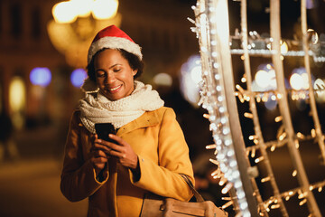 Fototapeta na wymiar Black Woman Using Smartphone In The City At Christmas Time