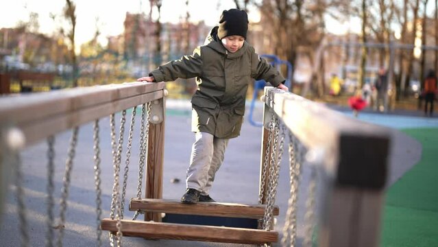 Child swings on swing in playground, pushes off with his feet and bounces. Happy smile and laughing on face and enjoy outdoors nature landscape. Leisure activity on childhood. Rest and relax.