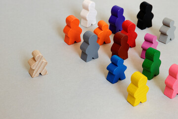 Wooden figures: one colorless person walking alone and colorful people standing together.