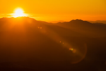 Orange and yellow sunset with mountains silhouettes. Gradient vivid nature background.
