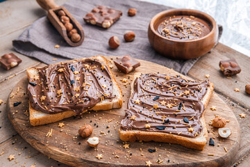 Board of bread with chocolate paste and hazelnuts on wooden background