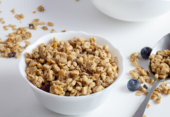 Granola is in a white plate. On a white background. There is a spoon next to it.