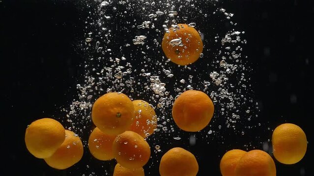 Close-up of mandarins falling down into the water against a black background in a slow motion.