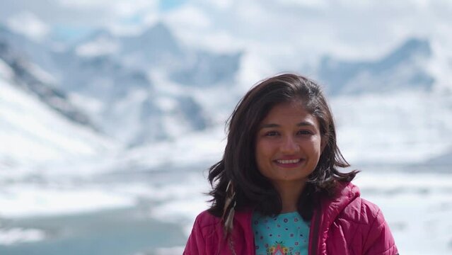 Portrait of Indian tourist girl in snow covered mountains looking at camera at Shinku La Pass, India. Winter holiday concept. Beautiful woman in background of snowy mountains during winter day.