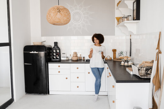 Cozy morning of african american girl on the kitchen at home. Attractive african woman with coffee and cake on the white kitchen.