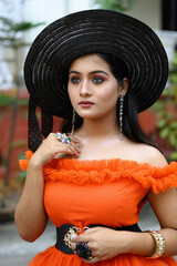 Portrait of young beautiful Indian woman wearing modern Western outfit with a black straw hat, posing fashionably against a blurred background