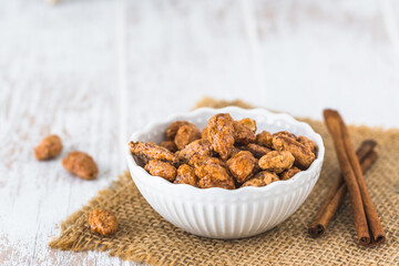 Bowl of sweet candied almonds on white rustic wooden background