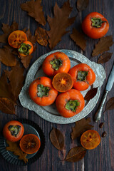 Vertical composition. Ripe appetizing persimmon fruits on a plate on a dark wooden background. Autumn fruits
