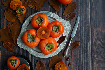 Ripe persimmon fruits on a plate, top view. Wooden background, copy space