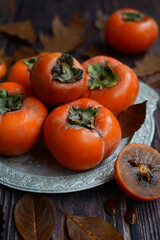 Close up of ripe orange persimmons on a silver platter. Vertical.