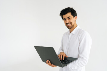 Studio portrait of cheerful young man in shirt posing with laptop computer and looking at camera standing on white isolated background. Friendly freelancer male holding notebook, copy space.