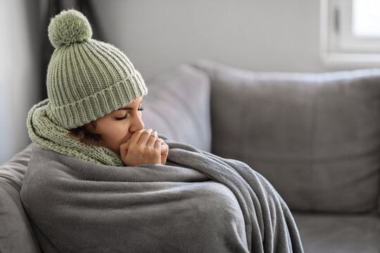 Freezing Woman Warming Hands With Breath While Sitting On Couch At Home