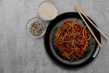 Spicy udon with chicken on a black plate and spices in glass bowls. View from above