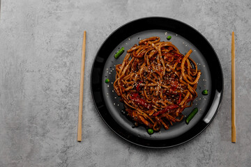 Spicy udon with chicken on a black plate on a gray concrete background. View from above