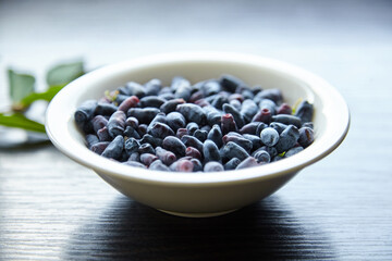 Fototapeta na wymiar Fresh honeyberry (Lonicera caerulea) in white bowl on wooden table. Blue haskap berry with green leaves