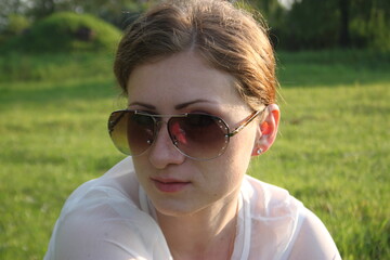 young woman in sunglasses sitting on green grass