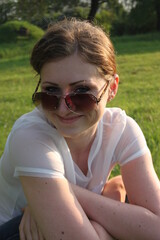 young woman in sunglasses sitting on green grass